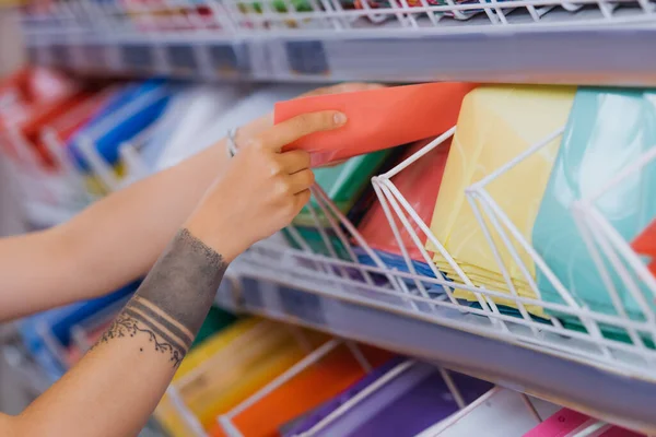 Partial view of tattooed woman taking plastic folder from rack in stationery shop — Fotografia de Stock