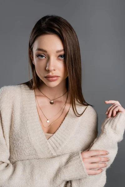 Pretty young woman in golden necklaces and soft sweater looking at camera isolated on grey — Foto stock