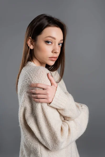 Brunette woman in soft sweater hugging herself and looking at camera isolated on grey — Photo de stock