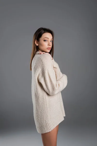 Young woman in long and warm sweater looking at camera on grey background — стоковое фото