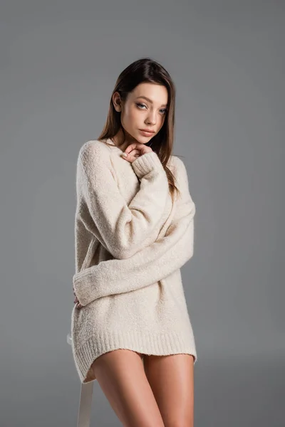 Pretty brunette woman in warm sweater hugging herself and looking at camera isolated on grey — Foto stock