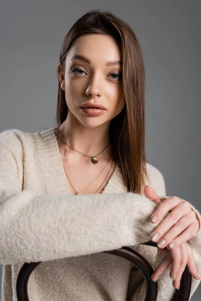 Young woman in warm sweater and golden necklaces looking at camera isolated on grey — Stock Photo