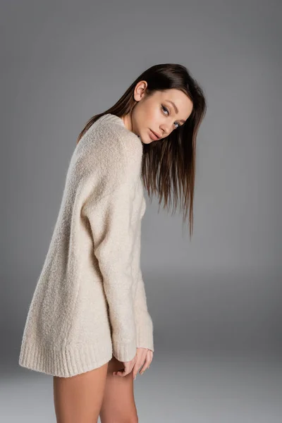 Brunette woman in long and soft sweater looking at camera on grey background — Foto stock