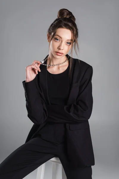 Fashionable woman in black clothing holding silver necklace isolated on grey — Stockfoto