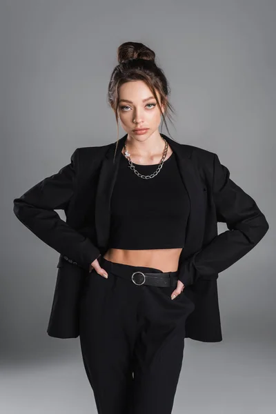 Pretty woman in crop top and black suit standing with hands on hips isolated on grey — Stock Photo