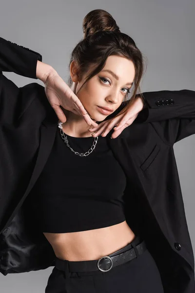 Pretty woman in black clothes and silver necklace posing with hands near face isolated on grey — стоковое фото