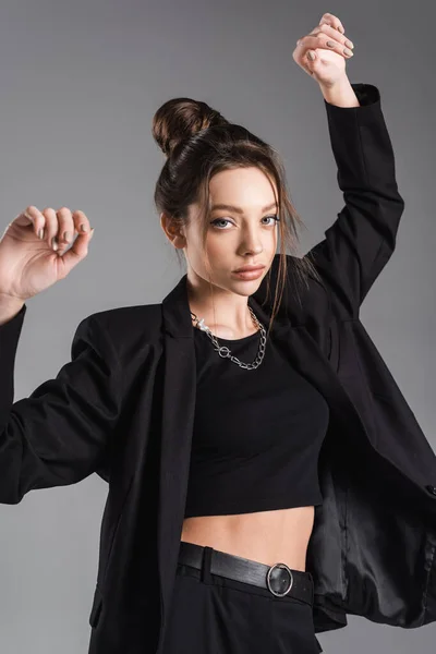 Woman in black clothes standing with arms up and looking at camera isolated on grey — Photo de stock