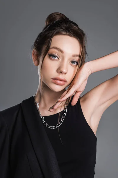 Young woman with makeup and silver necklace posing with hand near face isolated on grey - foto de stock