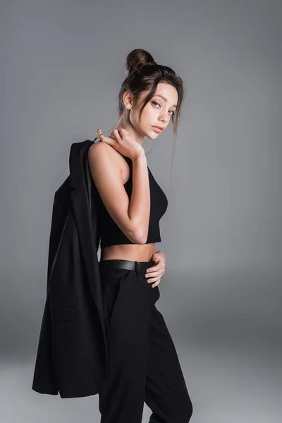 Young woman holding black blazer and looking at camera isolated on grey — Stockfoto