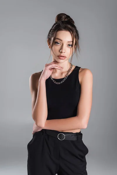 Pretty woman in black crop top holding hand near chin while posing isolated on grey — стоковое фото