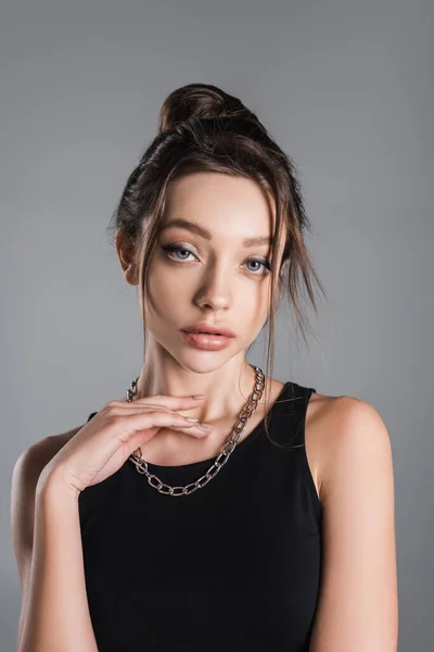 Pretty woman with makeup posing with hand near neck with silver necklace isolated on grey - foto de stock