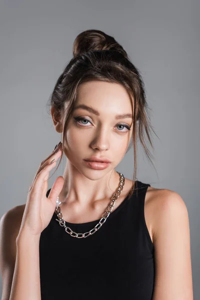 Sensual young woman in silver necklace touching face with makeup isolated on grey — стоковое фото