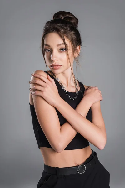 Trendy woman with makeup and silver necklace posing with crossed arms isolated on grey — Stock Photo