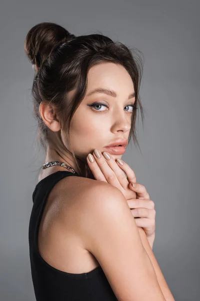 Stylish woman with makeup touching face and looking at camera isolated on grey — Stock Photo