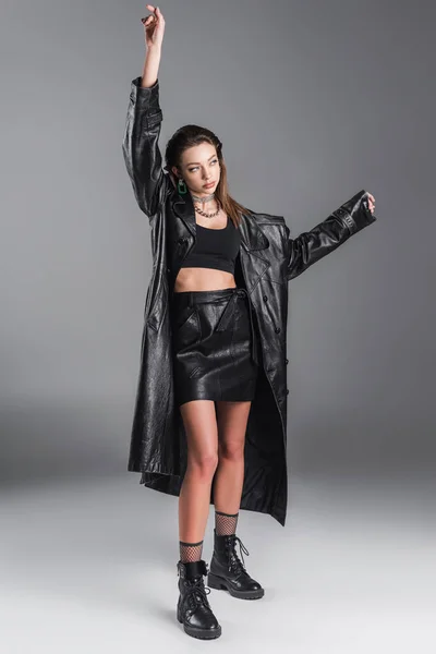 Full length of slender woman in black skirt and leather coat posing with arm up on grey background — Photo de stock