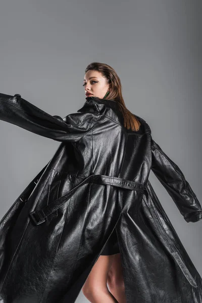 Young fashionable woman posing in black leather coat isolated on grey — стоковое фото