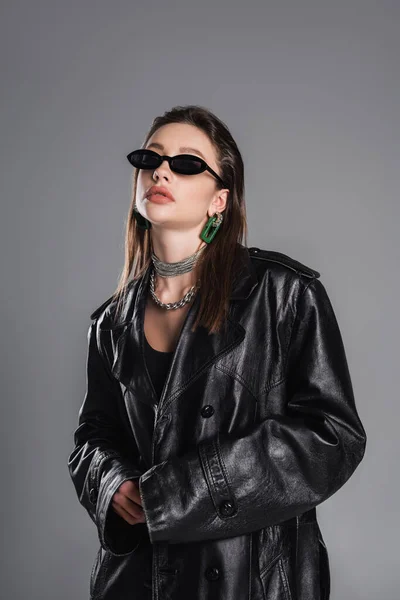 Brunette woman in trendy sunglasses and black leather coat posing isolated on grey — Foto stock