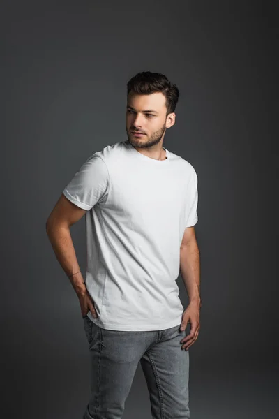 Young man in white t-shirt and jeans looking away isolated on grey — Stockfoto