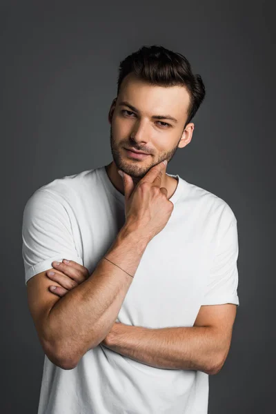 Portrait of brunette man in white t-shirt holding hand near chin isolated on grey — Stockfoto