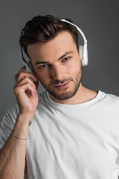 Портрет человека в белой футболке, слушающего музыку в наушниках, изолированных на сером — стоковое фото
