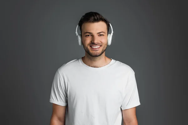 Happy man in white t-shirt and headphones looking at camera isolated on grey - foto de stock