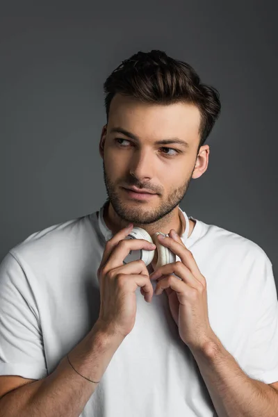 Portrait of bearded man holding headphones and looking away isolated on grey — Photo de stock