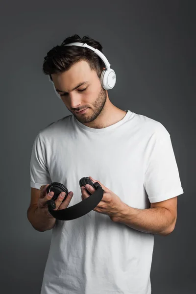 Брюнет у футболці дивиться на бездротові навушники, ізольовані на сірому — стокове фото