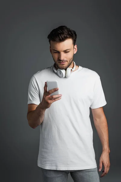 Young man with headphones using mobile phone isolated on grey — Stock Photo