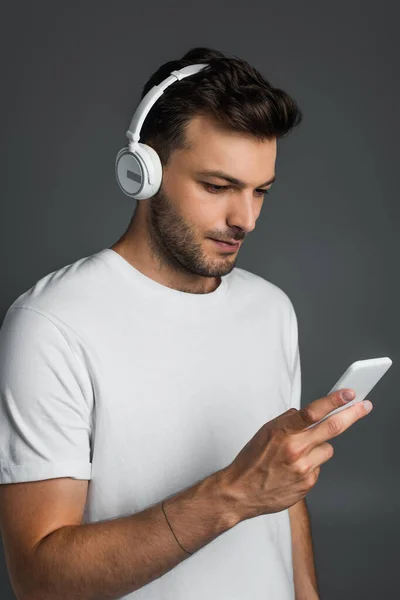 Бородатий чоловік використовує смартфон і навушники ізольовані на сірому — стокове фото