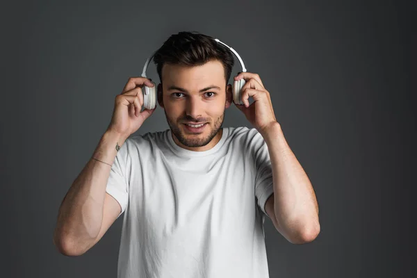 Smiling man in white t-shirt holding headphones near ears isolated on grey — Stock Photo