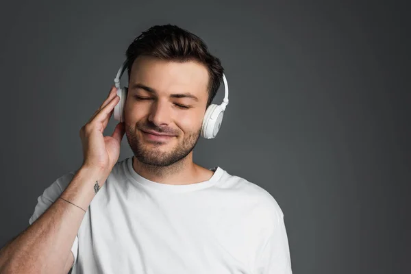 Чоловік з закритими очима слухає музику в навушниках ізольованих на сірому — стокове фото