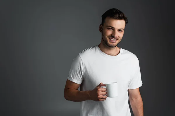 Cheerful man in white t-shirt holding cup of coffee isolated on grey — Stockfoto