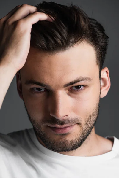 Portrait of young man touching hair and looking at camera isolated on grey — Stock Photo