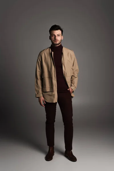 Full length of stylish man in jacket looking at camera on grey background — Fotografia de Stock