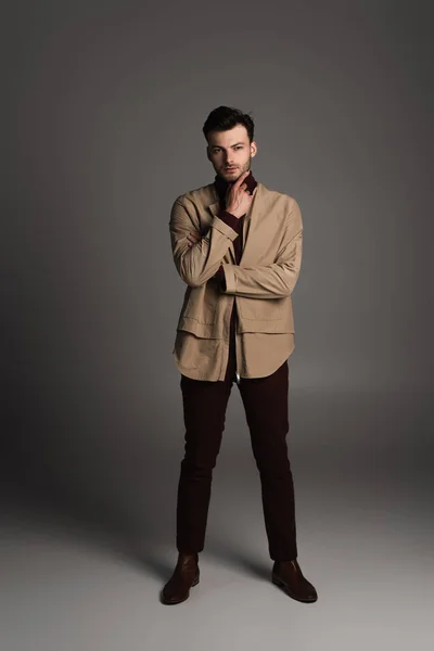 Full length of stylish man in autumn outfit touching chin on grey background — Stock Photo