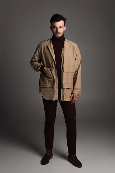 Young brunette man in autumn jacket standing on grey background — Photo de stock