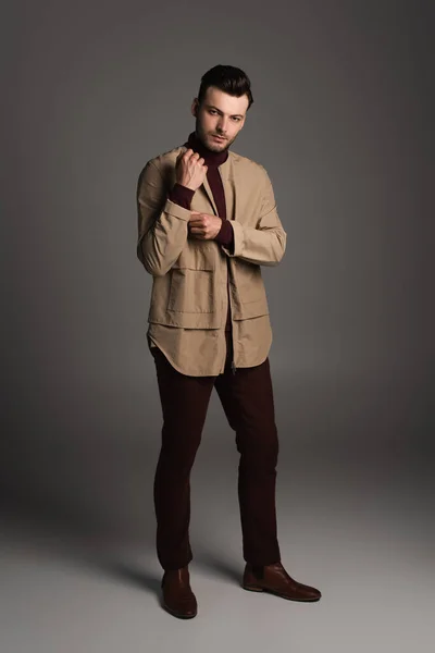 Full length of stylish young man in jacket looking at camera on grey background — Fotografia de Stock