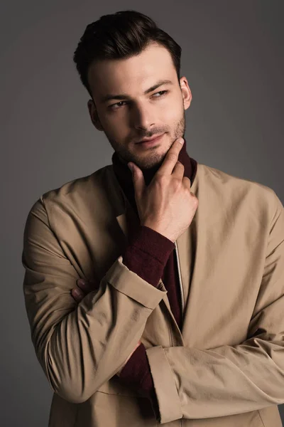 Portrait of trendy man in autumn jacket and turtleneck touching chin isolated on grey — Stock Photo