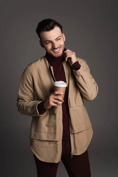 Cheerful man in autumn jacket and turtleneck holding coffee to go isolated on grey — Fotografia de Stock