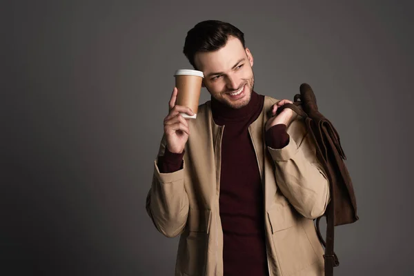 Positive man in autumn outfit holding backpack and paper cup isolated on grey — Stock Photo