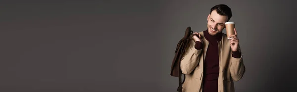 Cheerful man in autumn jacket holding backpack and coffee to go isolated on grey, banner — Stock Photo