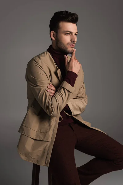 Pensive stylish man in autumn outfit sitting on chair isolated on grey — Photo de stock