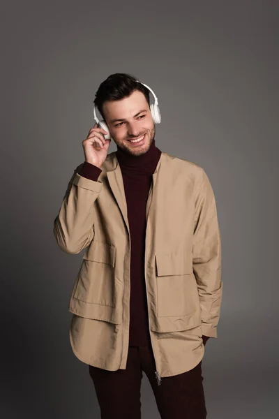 Smiling man in autumn outfit listening music in headphones isolated on grey - foto de stock