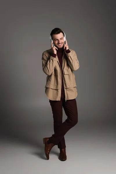 Full length of stylish man in autumn outfit and headphones standing on grey background - foto de stock