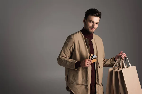 Man in brown jacket holding shopping bags and credit cards isolated on grey — Foto stock