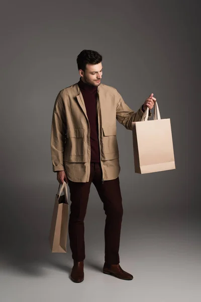 Stylish man in autumn jacket looking at shopping bag on grey background — Stockfoto