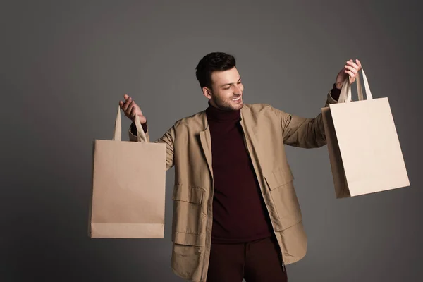 Happy man in autumn outfit holding shopping bags isolated on grey — Stock Photo