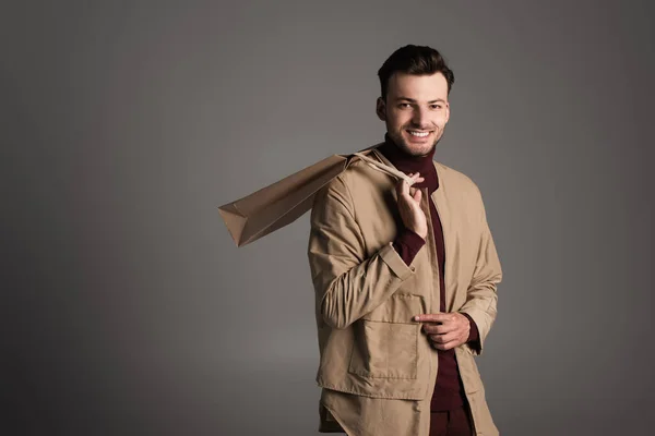 Cheerful young man in autumn outfit holding shopping bag isolated on grey - foto de stock