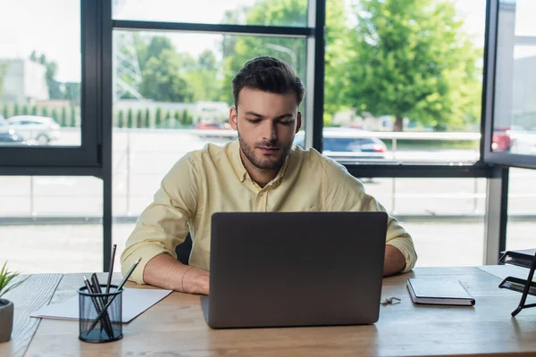 Young manager using laptop near papers and stationery in office — Fotografia de Stock