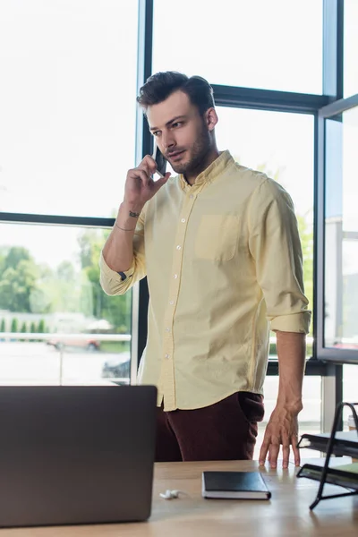 Businessman talking on smartphone near laptop and notebook on table in office — Fotografia de Stock